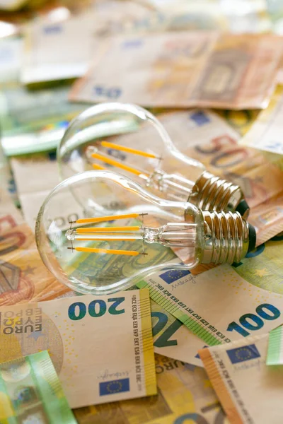 Electricity cost.Rising electricity prices in Europe.Crisis of energy production in the EU countries.Increasing the cost of light and heat.Saving electricity concept.Two light bulbs on euro bills.
