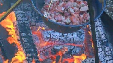Meat on the fire.Cooking meat in a cauldron.Wood fire and cauldron with food. Meat pieces in a cauldron on burning coals background.Cooking outdoors and on the go. 4k footage
