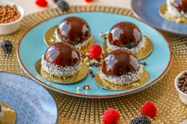  Mavi tabakta ahududu soslu kek ve bej bir masada çikolata dekoru. Böğürtlenli tatlı. Nefis, havadar pasta suflesi..