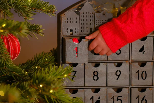 advent calendar.santa claus in hand on christmas advent calendar background.child hand in a sweater opens the advent calendar near Christmas tree with toys.Gifts and surprises for Christmas