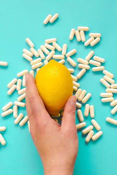 Taking vitamin C tablets.capsules of vitamin C in a hand and yellow lemon citrus fruits on a blue background.View from above.Health and medicine concept