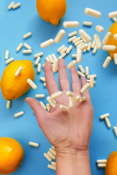 Vitamin C.Taking vitamin C tablets.White capsules of vitamin C in a hand and yellow lemon citrus fruits on a blue background.Tablets fly into the hand.