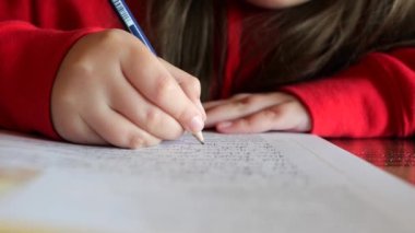 Ev ödevi. Liseli kız ödevini yapıyor. Çocuk not defterine kurşun kalemle yazıyor. Eğitim ve eğitim kavramı. Çocukça bir eldeki yakın plan kalem deftere kelimeler yazıyor. 4k görüntü