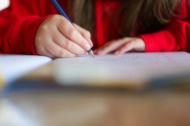 Çocuk not defterine kurşun kalemle yazıyor. Çalış ve öğren. Öğrenci kız ödevini yapıyor. Çocukça bir eldeki yakın çekim kalemi bir deftere kelimeler yazar. 