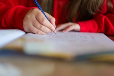 Çocuk not defterine kurşun kalemle yazıyor. Ödev. Ders ve eğitim. Okul kızı ödevini yapıyor. Çocukça bir eldeki yakın çekim kalemi bir deftere kelimeler yazar. 