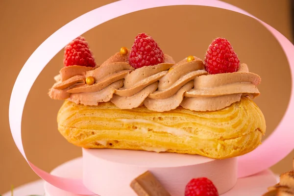 茶色の背景に表彰台にチョコレートクリームとラズベリーとケーキを消去します カスタードケーキ — ストック写真