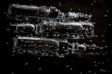 Siyah bir arka planda suda kabarcıklarda kozmetik ampulleri. Kozmetik tıbbi ve bakım konsepti.