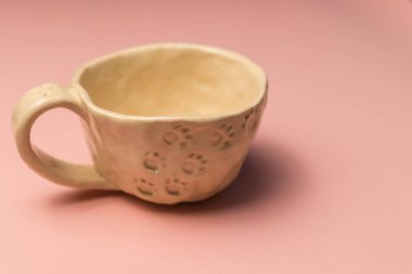 Pembe arka planda boş bir bej el yapımı kil bardak. Uzayı kopyala Kupa kedi pençesi şeklinde bir desenle süslenmiş. Ev konforu. 