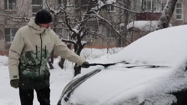 Een Man Verwijdert Sneeuw Uit Een Auto Met Een Borstel — Stockvideo