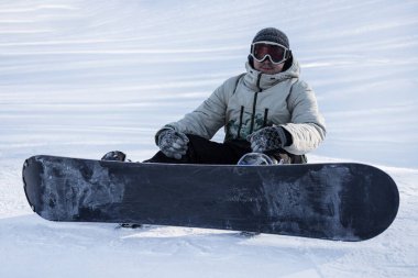 Bir snowboardcu bir dağın tepesinde oturuyor. Kış sporları: snowboard ve yokuş aşağı kayak. Kayak merkezlerinde tatiller