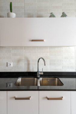 Mutfak lavabosu beyaz dolaplar ve siyah mermer kapaklı. Doğal ışık.