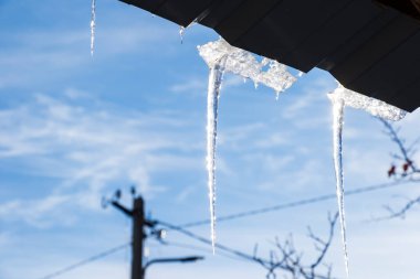Çatıda buz saçakları, mavi gökyüzü ve buzlu su, kış buzu.