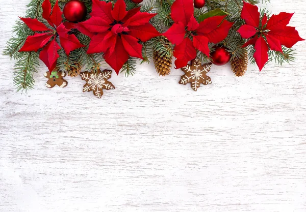 Noel toplarıyla Noel ağacı, zencefilli Noel ekmeği, kırmızı noktalı çiçekler ve beyaz ahşap bir arka planda beyaz ladin çiçekleri. Üst manzara, düz uzanma