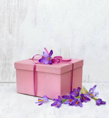 Pink gift box with flowers violet crocuses on a white table with space for text. Holiday spring composition