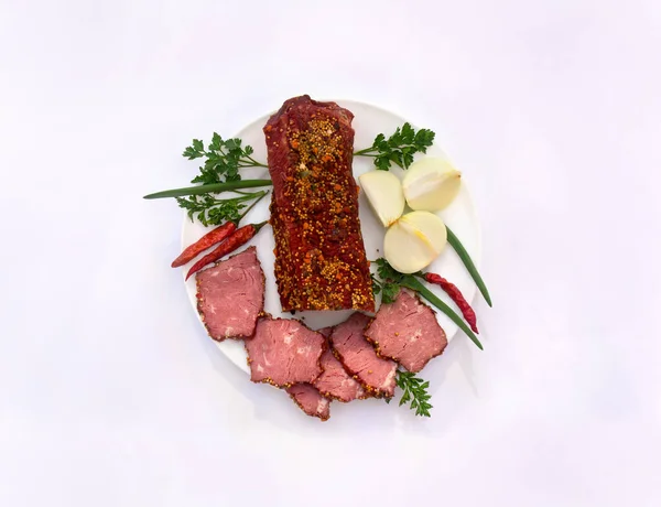 Smoked beef with pieces and spice, mustard, red chilli pepper, bulb onion and green leaves onion and parsley on white plate on light background. Top view, flat lay
