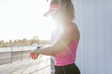 Genç bir spor kızı elindeki akıllı saate bakar ve nabzını kontrol eder, koşudan sonra mola verir..