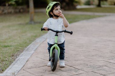 Kasklı küçük çocuk şehir parkında bisiklet sürüyor. Neşeli çocuk dışarıda