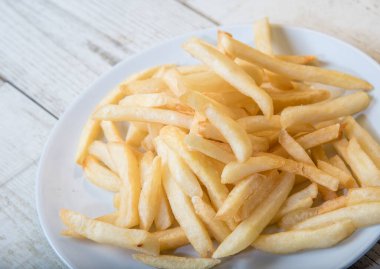 Ahşap tabakta beyaz bir tabakta patates kızartması, barbekü sosu, domates sosu.