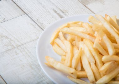 Ahşap tabakta beyaz bir tabakta patates kızartması, barbekü sosu, domates sosu.