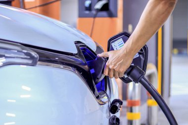 İnsan eli elektrikli arabayı tutuyor. Aracın elektriklenmesi için şarj aletini prize takıyor.