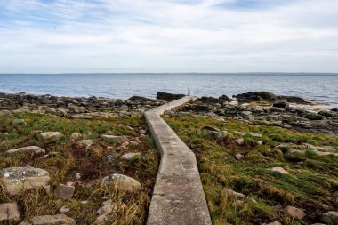 Beton iskeleli kayalık bir kıyı şeridi. Arka planda mavi bir su ve mavi bir gökyüzü. Fotoğraf: Skalderviken, İsveç
