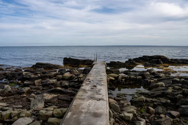 A rocky shoreline with a concrete jetty. Blue water and a blu sky in the background. Picture from Skalderviken, Sweden — Stock Photo, Image