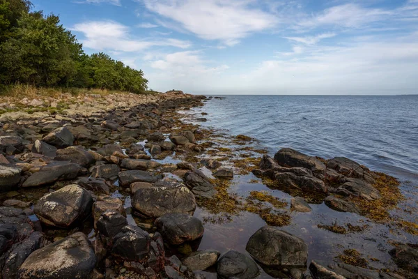 A rocky shoreline with blue water and a blu sky in the background. Picture from Skalderviken, Sweden — Stock Photo, Image