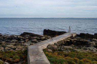 Beton iskeleli kayalık bir kıyı şeridi. Arka planda mavi bir su ve mavi bir gökyüzü. Fotoğraf: Skalderviken, İsveç