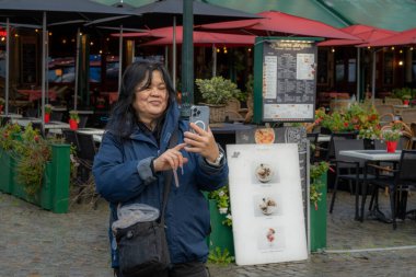 Asyalı bir kadın restoranın önünde selfie çekiyor. Fotoğraf pazar meydanından, Grote Markt, Bruges, Belçika.