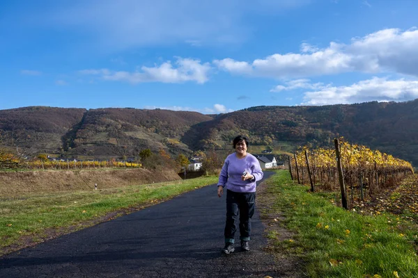 Una mujer en un camino que pasa por un distrito vinícola en el valle del Mosel. Hermosas hojas de vid amarilla y hierba verde — Foto de Stock