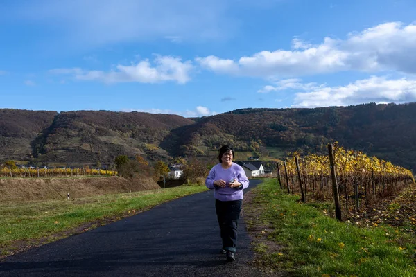 Una mujer en un camino que pasa por un distrito vinícola en el valle del Mosel. Hermosas hojas de vid amarilla y hierba verde — Foto de Stock