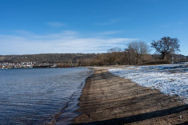 Um lago praia de inverno coberto de neve e um céu azul no fundo — Fotografia de Stock