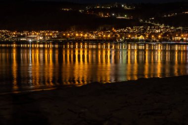 Lights from a hillside town reflect in a lake at night