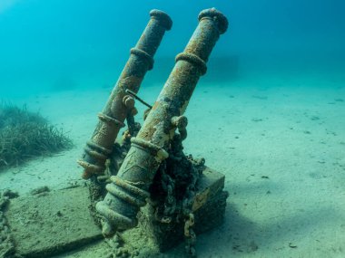 Antique cannons on a sandy sea floor. Beautiful turquoise water in the background