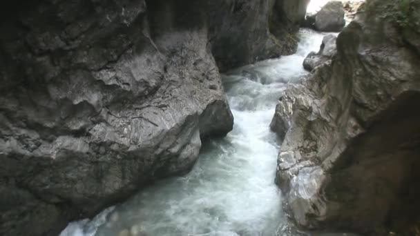 山の川は狭い岩の間を流れている 水は岩の上で激しく壊れ 泡立ち 動き続けています 水の近くの岩そのもの 水が石を破った 野生の自然 — ストック動画