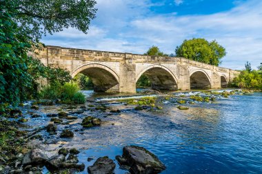Yazın İngiltere 'nin Yorkshire, Ripon kenar mahallelerindeki Ure Nehri üzerindeki eski bir ortaçağ köprüsüne doğru kayalık sahil manzarası