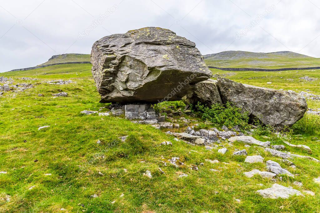 A view of a masive glacial erratic boulder resting on limestone pavement on the southern slopes of Ingleborough, Yorkshire, UK in summertime