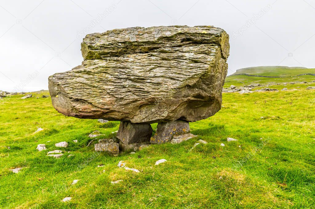 A side view showing a glacial erratic supported on the limestone pavement on the southern slopes of Ingleborough, Yorkshire, UK in summertime