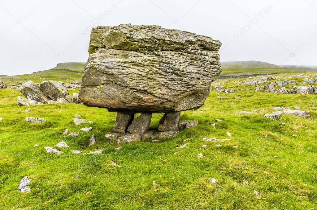 A view showing a glacial erratic supported on the limestone pavement on the southern slopes of Ingleborough, Yorkshire, UK in summertime