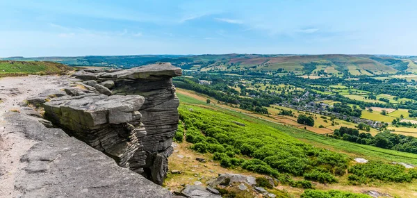 A panorama view of overhanging rock slabs and the Hope Valley from the top of Bamford Edge, UK in summertime