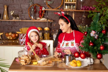Anne ve kızı karanlık bir mutfakta yılbaşı için zencefilli kurabiye pişiriyor ve Noel Baba şapkasıyla gülümsüyor.