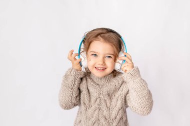 Beyaz arka planda kulaklıklı küçük bir kız müzik dinliyor ve mesajlaşmak için mekanın tadını çıkarıyor.