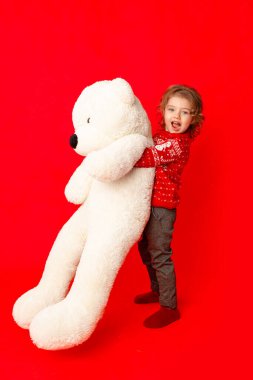 Çocuğum, kışın giydiği büyük oyuncak ayıyla kırmızı arka planda küçük bir kız, mesaj atmak için yer var.