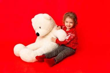 Kırmızı arka planda büyük bir oyuncak ayıyla küçük bir kız. Mesaj atmak için yer var.