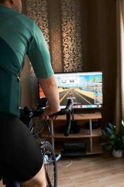 Cyclist is training on the bike with a TV doing online cycling. Stay fit and active while at home. Indoor cycling in winter.