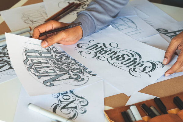 Типография Художник-каллиграф рисует эскиз письма, позволяя рисовать чернильные бумажные столы..