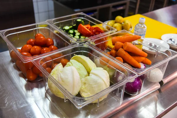 Vegetables - carrots, onions, cabbage, tomatoes, red peppers, cucumbers - in plastic containers in the kitchen