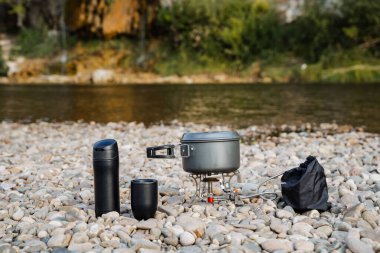 Yürüyüşe çıkmış bulaşıklar. Bir termos bardağı ve kayalıklarda bir tencere var. Kamptaki turist mutfağı. Nehir kıyısında tatil kavramı..
