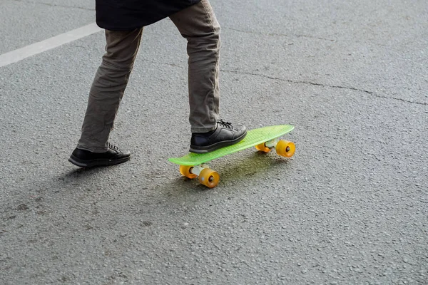 一个穿着外套和靴子的男人试图用黄色轮盘和滑板站在明亮的绿色上 一个嬉皮士在沥青路面上学习滑板 活动和新的娱乐活动 高质量的照片 — 图库照片