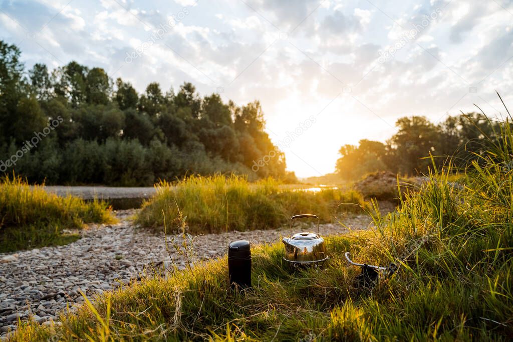 Dinner at sunset by the river. Meal in nature, dinner tourist. Cooking in the fresh air, hiking in the summer to the river. Thermos and kettle. Banks, forest and river. High quality photo